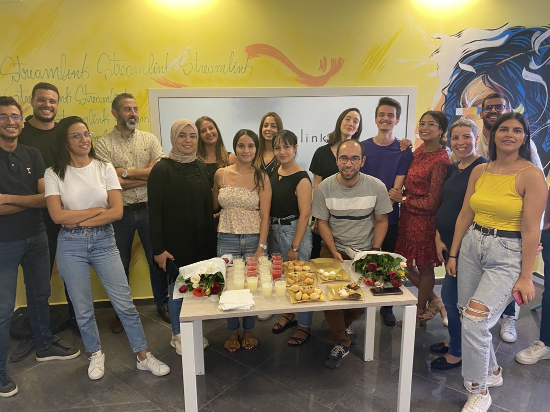 L'équipe Streamlink réunie autour d'une table, devant le mur peint aux couleurs de Streamlink